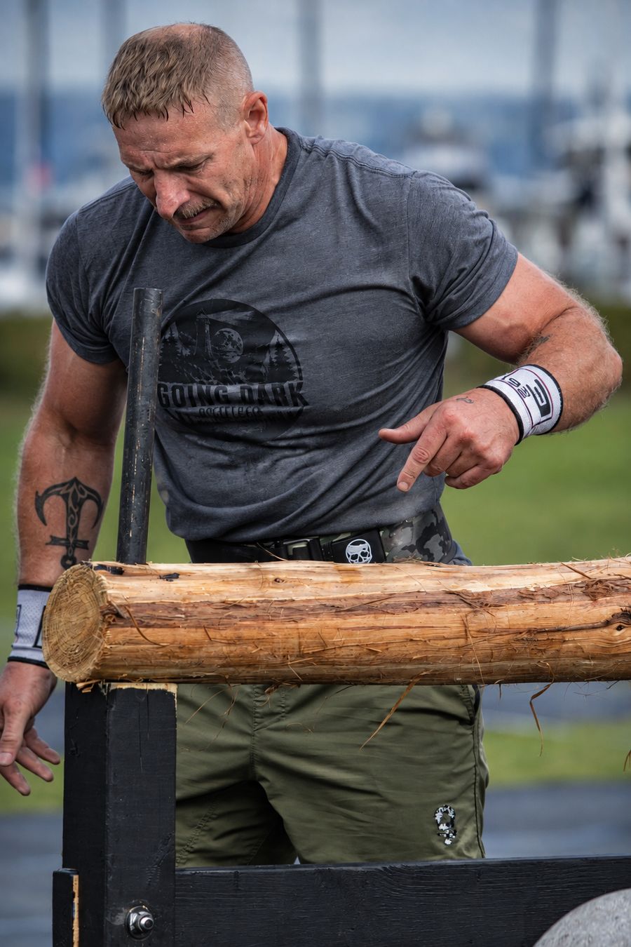 Toby carrying a log at a strength event, anchor tattoo on his forearm
